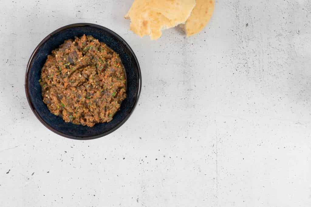 Marokkanischer Auberginensalat mit Kreuzkümmel und frischen Kräutern, daneben Fladenbrot