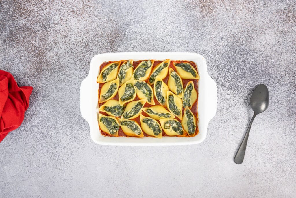 Nahaufnahme gebackener Muschelnudeln mit veganer Spinatfüllung in Tomatensauce