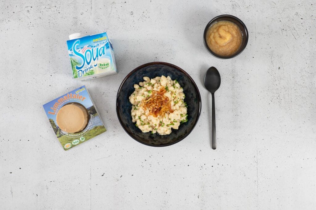 Vegane Chäshörnli mit Röstzwiebeln und Schnittlauch, daneben Apfelmus, Limmattaler und Bio-Soya-Drink von Soyana