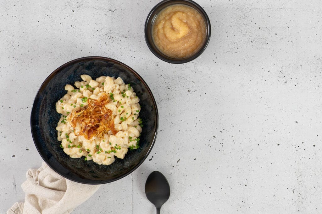 Vegane Chäshörnli ohne Kartoffeln mit Röstzwiebeln, Schnittlauch und einer Schüssel Apfelmus