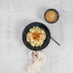 Vegane Chäshörnli mit Löffel im Teller, serviert mit Apfelmus und Leinenserviette