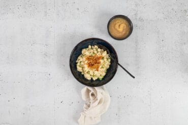 Vegane Chäshörnli mit Löffel im Teller, serviert mit Apfelmus und Leinenserviette