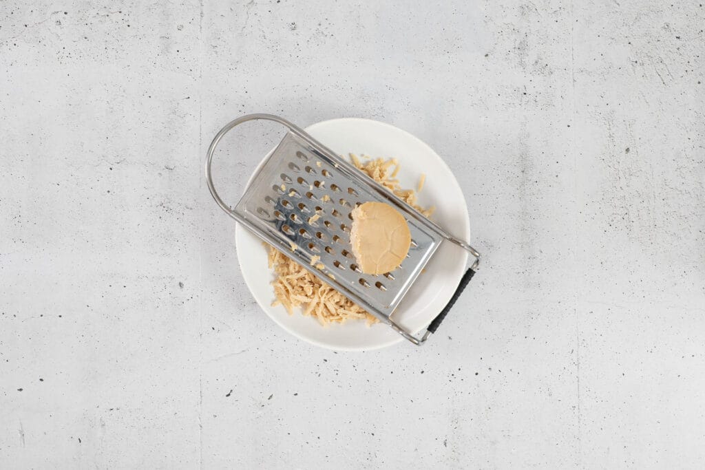 Veganer Käse Limmattaler wird für die Käsesauce frisch an der Raffel gerieben
