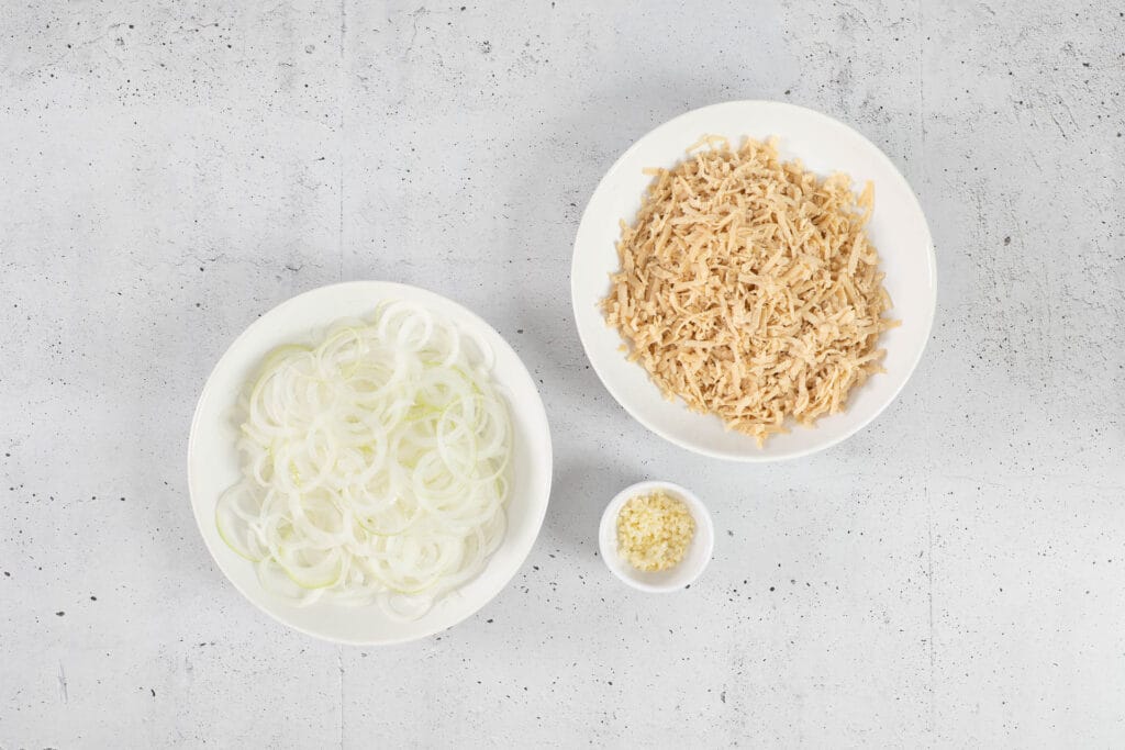 Vorbereitete Zwiebelringe für Röstzwiebeln, frisch geriebener veganer Käse und gehackter Knoblauch