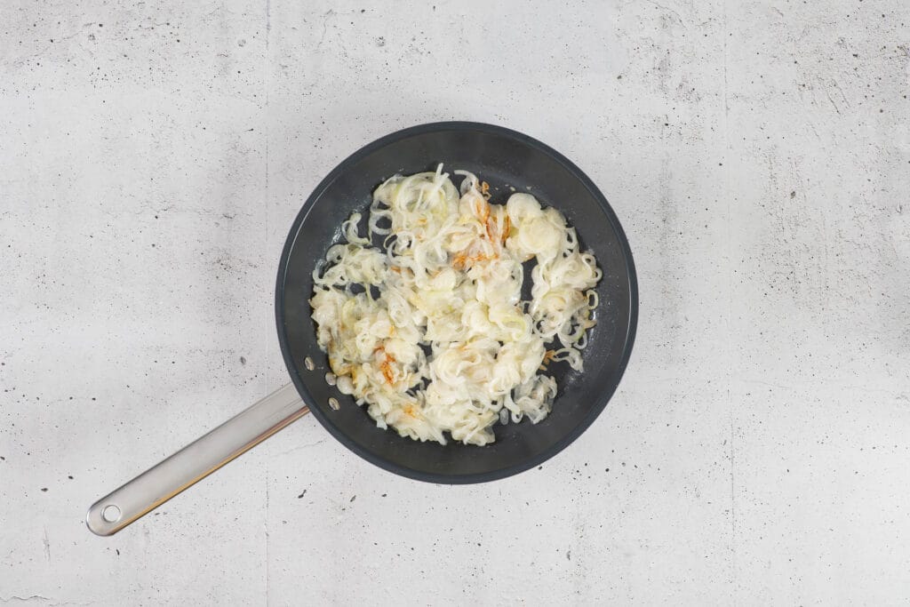 Bemehlte Zwiebelringe beginnen in der Bratpfanne zu rösten, als Röstzwiebeln für vegane Chäshörnli