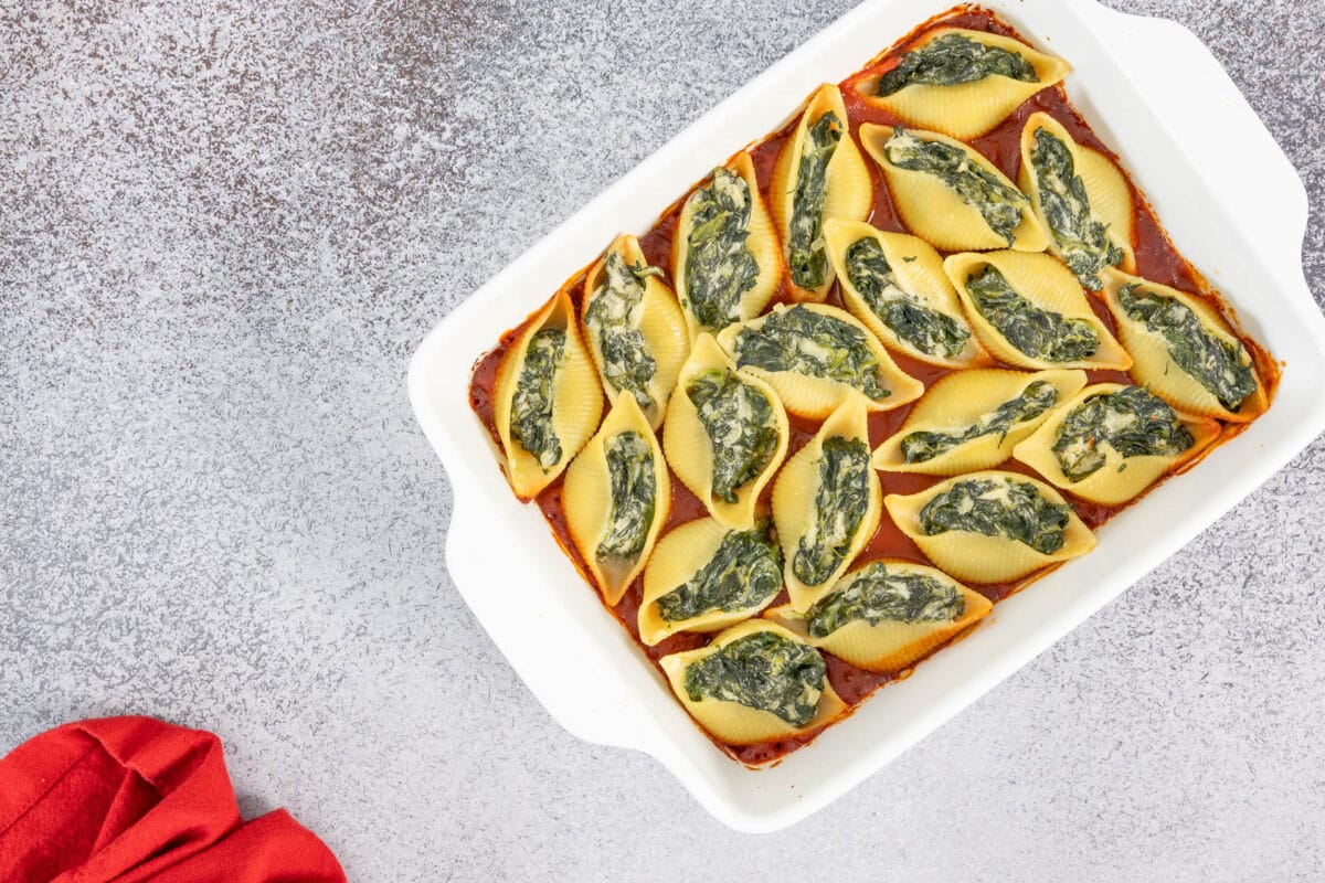 Gebackene Pastamuscheln mit Spinat-Frischkäse-Füllung in Tomatensauce, daneben eine rote Serviette