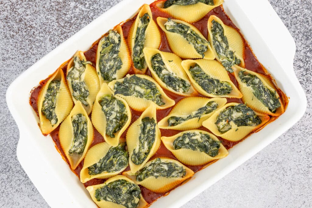 Nahaufnahme gebackener Muschelnudeln mit veganer Spinatfüllung in Tomatensauce